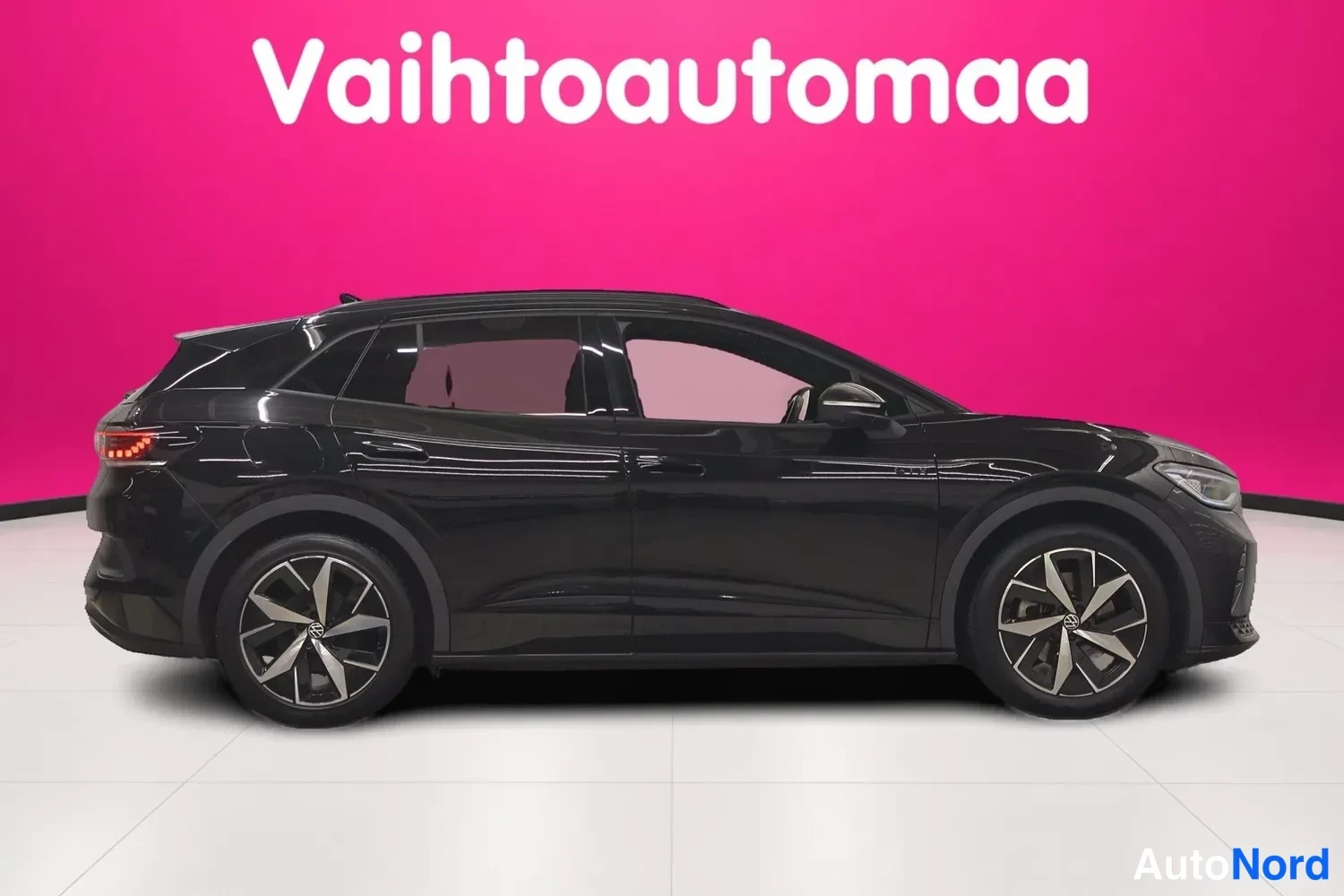 Sivulta: Musta VSP täsmälleen sivulta kuvattuna vasen kylki näkyvissä; kevytmetallivanteet, ovien kahvat ja tummat lasit erottuvat vaaleanpunaisen taustan edessä.