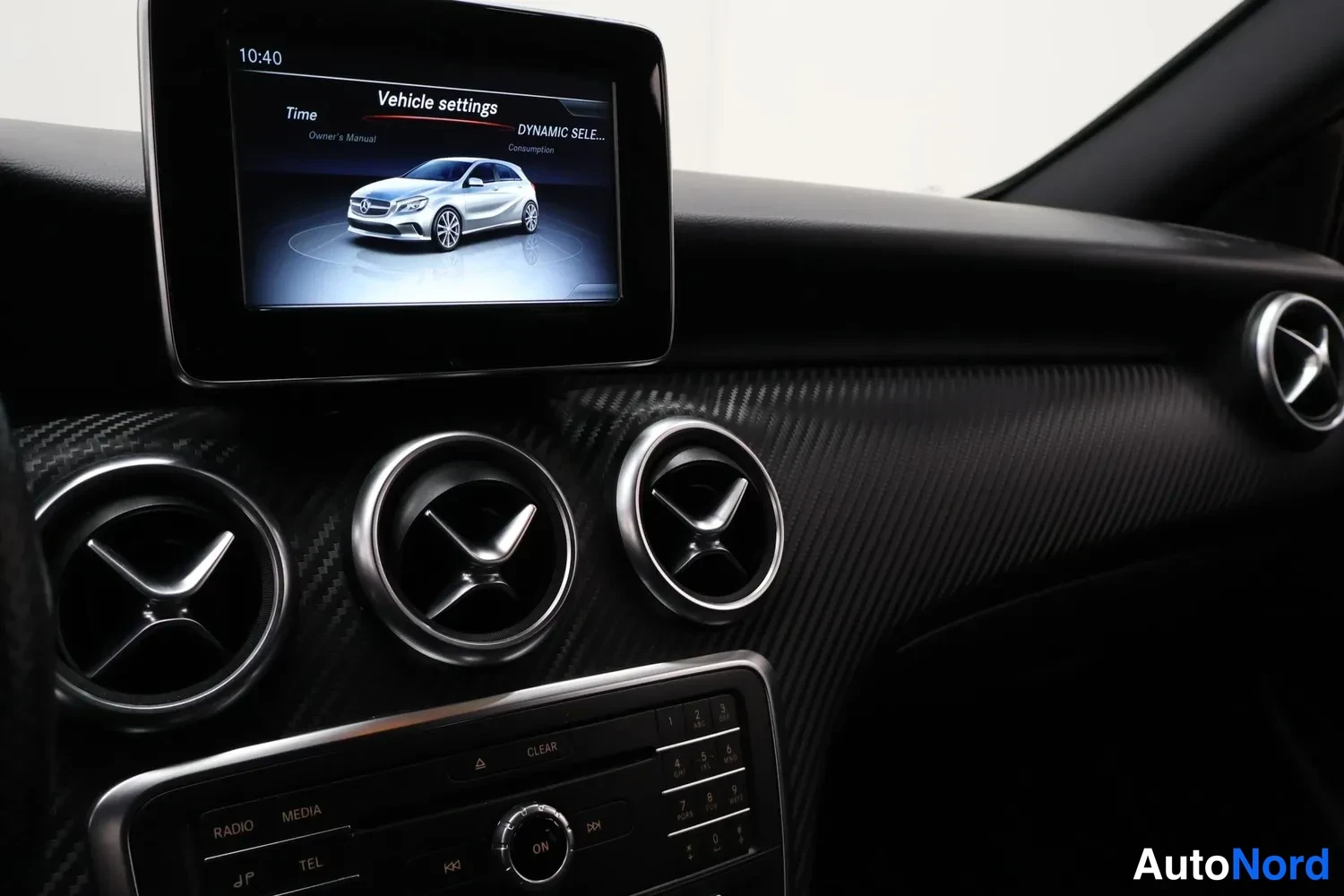 Muu: Kojelaudan keskialue, jossa kolme pyöreää ilmastointisuutinta, näytöllä Vehicle settings -valikko ja alla radio- ja numeronäppäimistö, CARBON-kuosinen pinta.