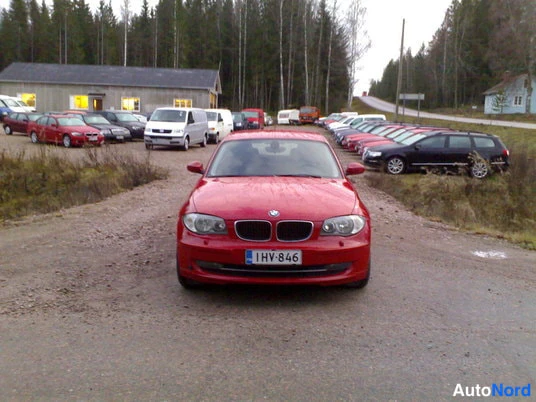 Edestä: Punainen henkilöauto edestä kuvattuna soratien varrella, rekisterikilpi.