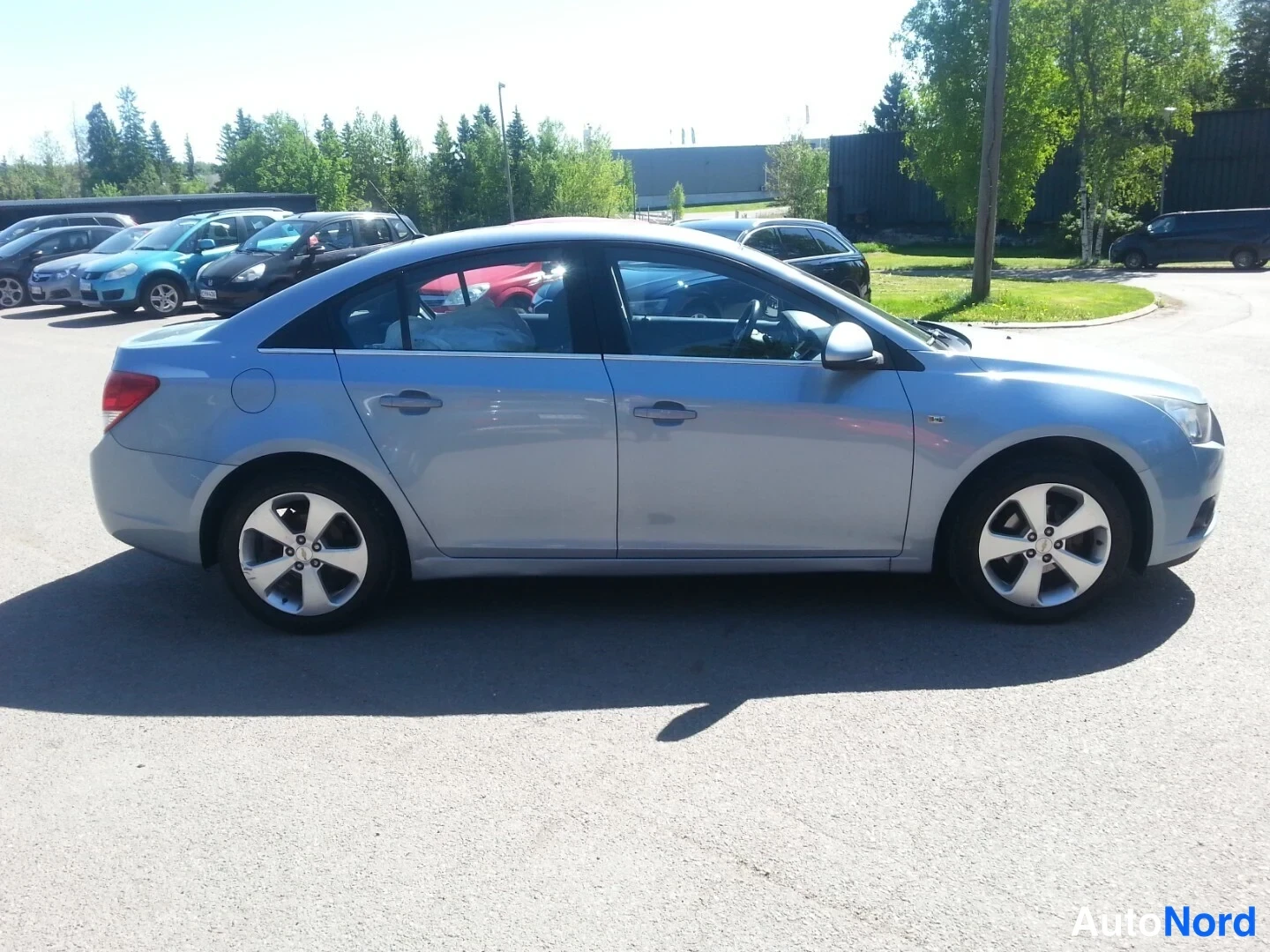 Etuviisto, nokka oikealle: Chevrolet Cruze -sedanin etukulma vasemmalta eteenpäin; sinertävänharmaa auto siisti auringonpaisteessa parkkipaikalla.