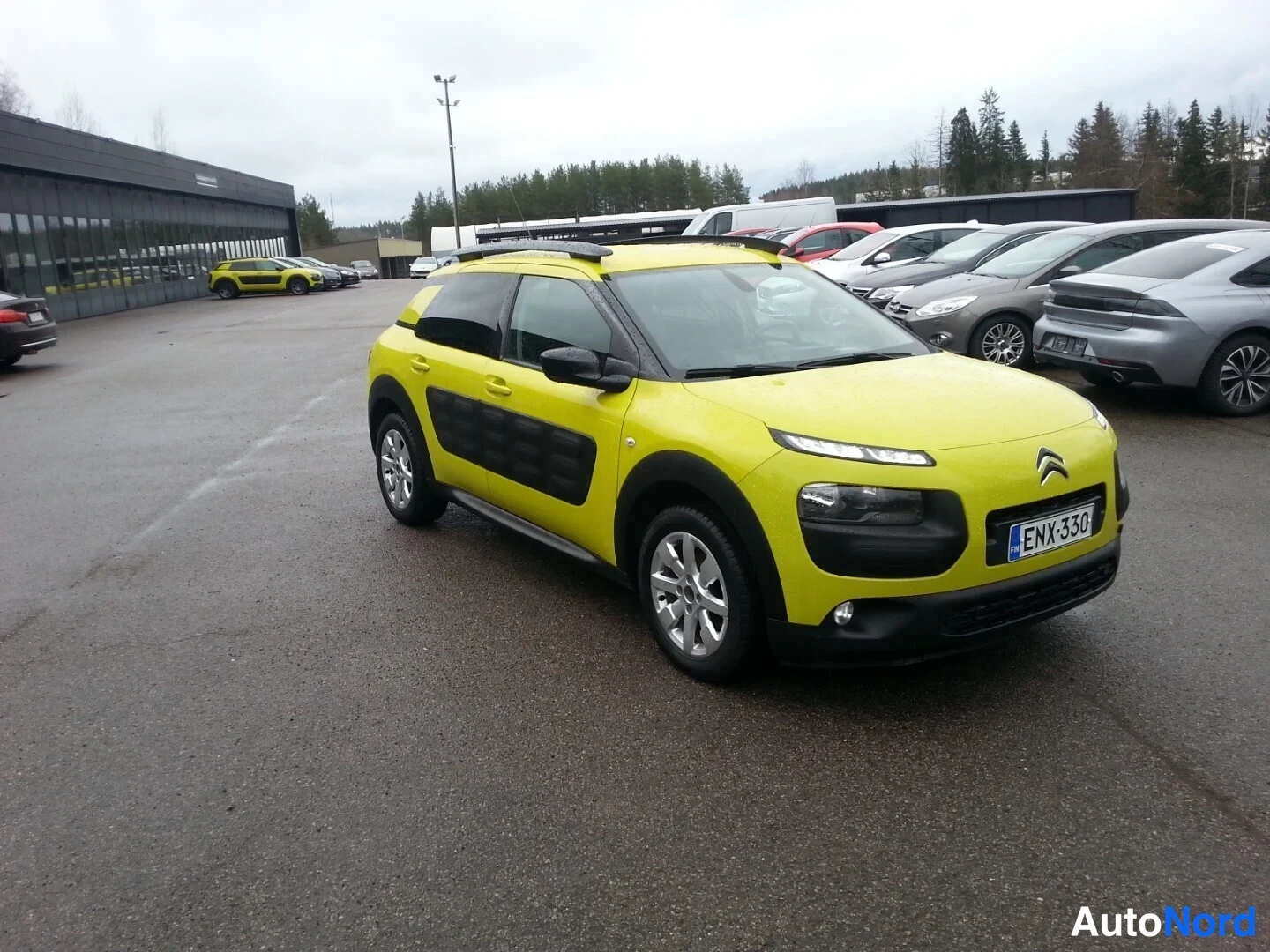 Etuviisto, nokka oikealle: Keltainen Citroën C4 Cactus -henkilöauto pysäköitynä autotallin pihoilla, etukulma oikealta kuvattuna.