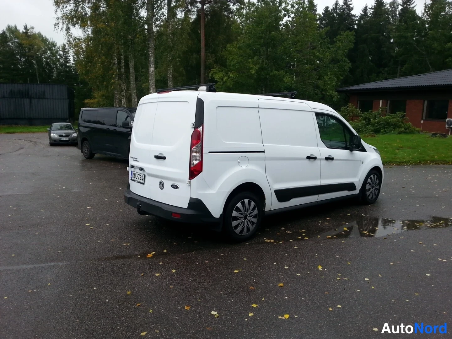 Takaviisto: Valkoinen pakettiauto takaviistosta asfalttipihalla