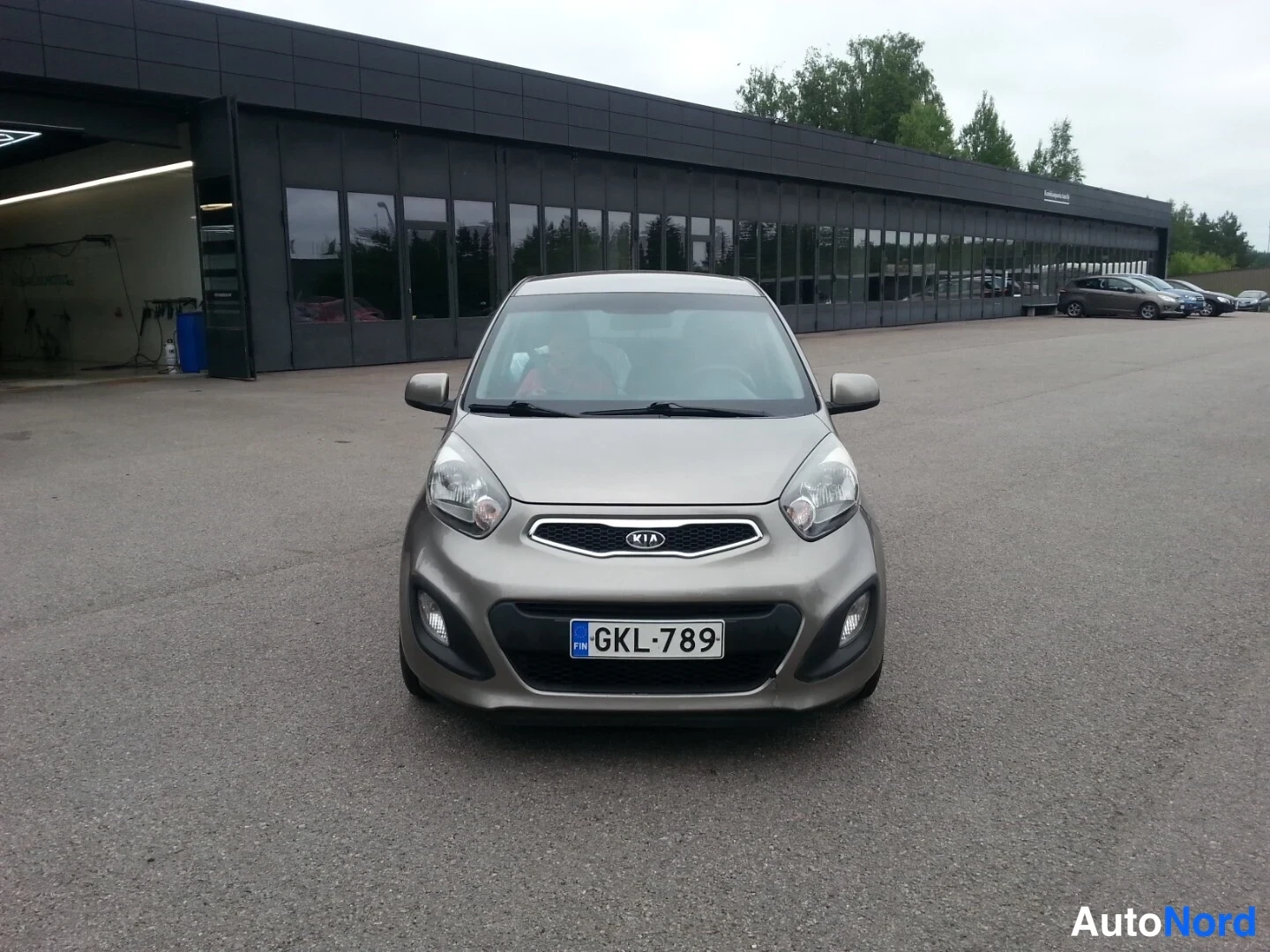 Edestä: Kia Picanto edestäpäin kuvattuna parkkipihalla harmaan rakennuksen edessä.