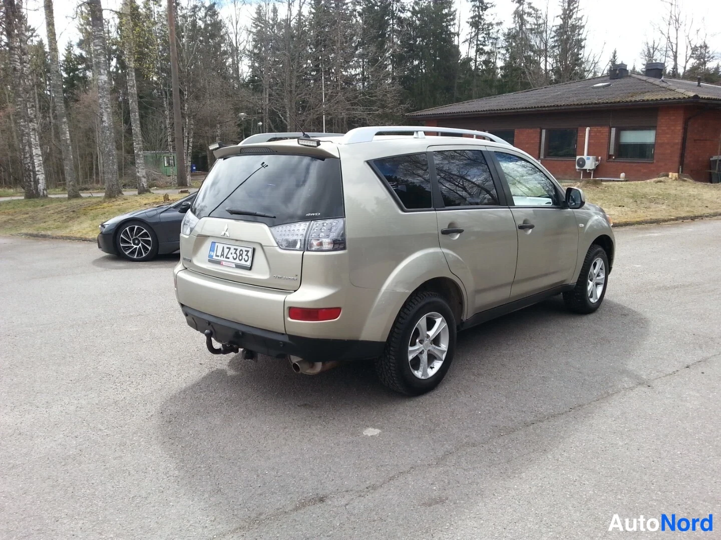 Takaviisto: Kultaharmaa Mitsubishi Outlander takaa vasemmalta kolmannelta kulmasta, rekisteritunnus ja hopeiset kattokaiteet.