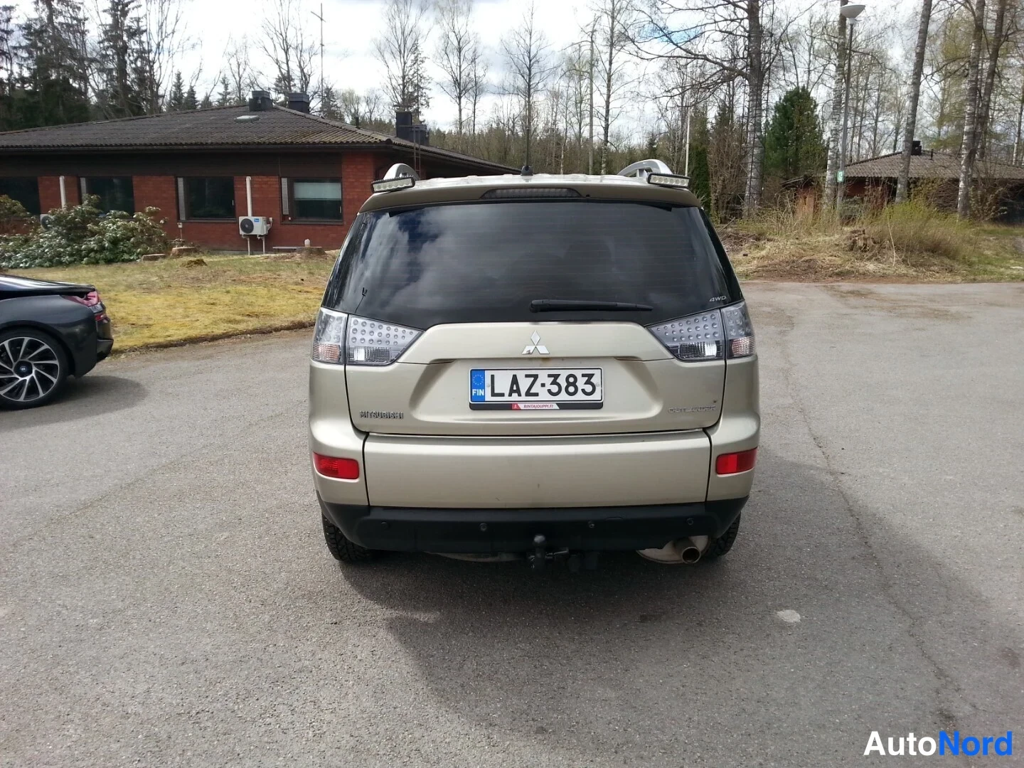 Takaa: Beige Mitsubishi Outlander takaa päin, rekisteritunnus, vetokoukku näkyvissä.