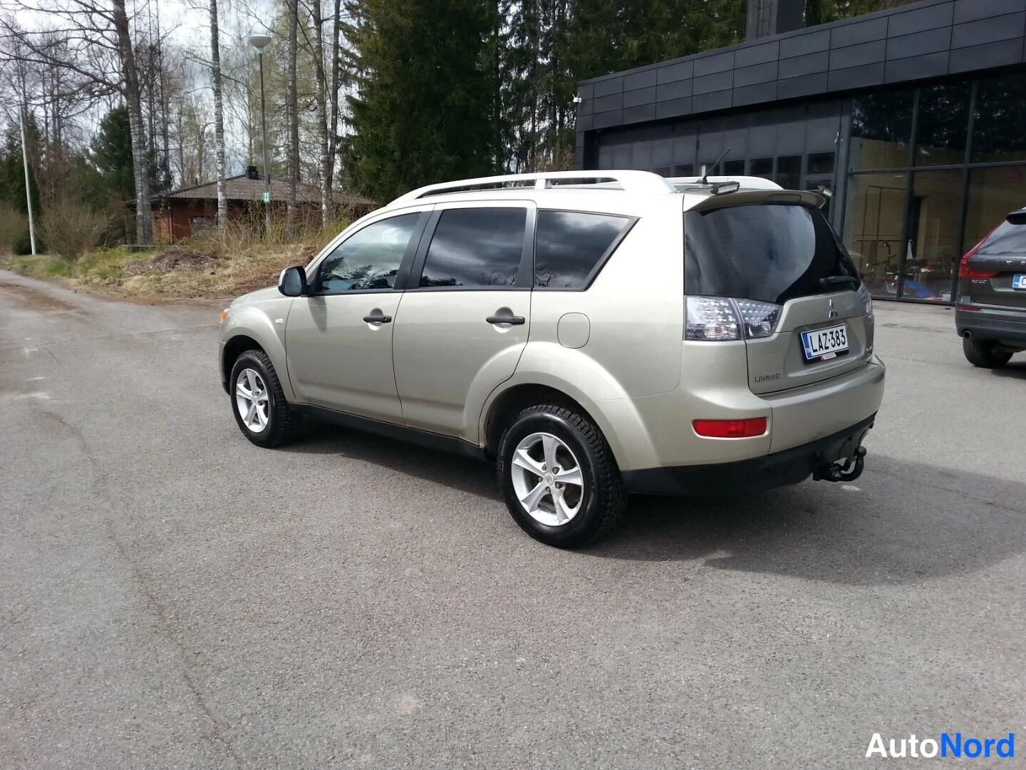 Takaviisto: Auto takaviisto vasemmalta: kultainen (beige) Mitsubishi Outlander -tyyppinen kattonelineellinen Maasturi, rek, vetokoukku takana, korin oikea sivu ja takaosa n