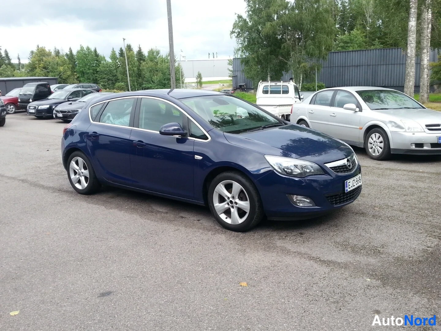Etuviisto, nokka oikealle: Opel Astra -henkilöauto tummansinisenä kuvattuna etuviistosta oikealta, etupuskuri, etuvojelot ja kylki näkyvissä.