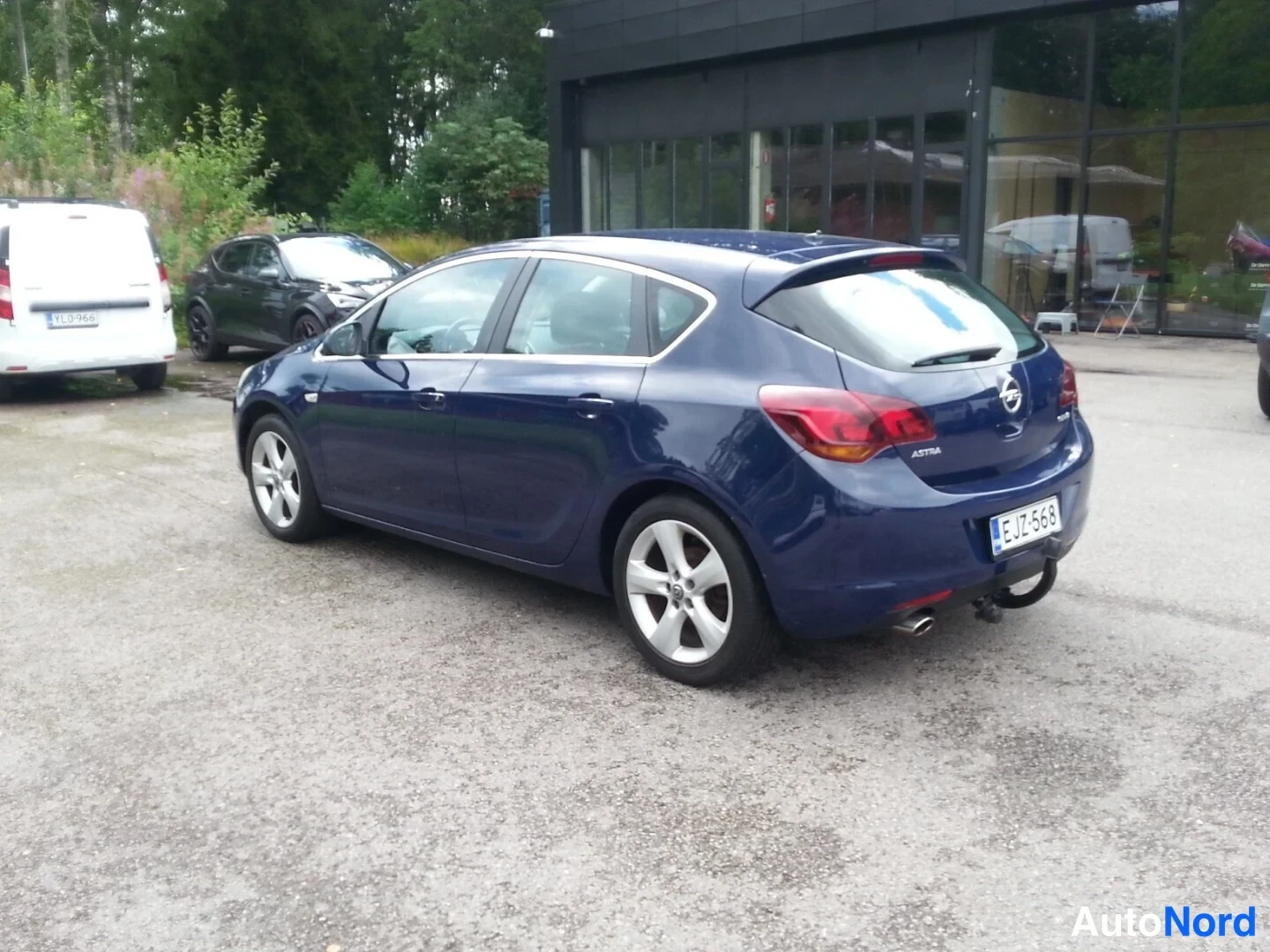 Takaviisto: Opel Astra -henkilöauto tummansinisenä kuvattuna taka viistosta vasemmalta, takavalot ja moottorinisti näkyvissä.