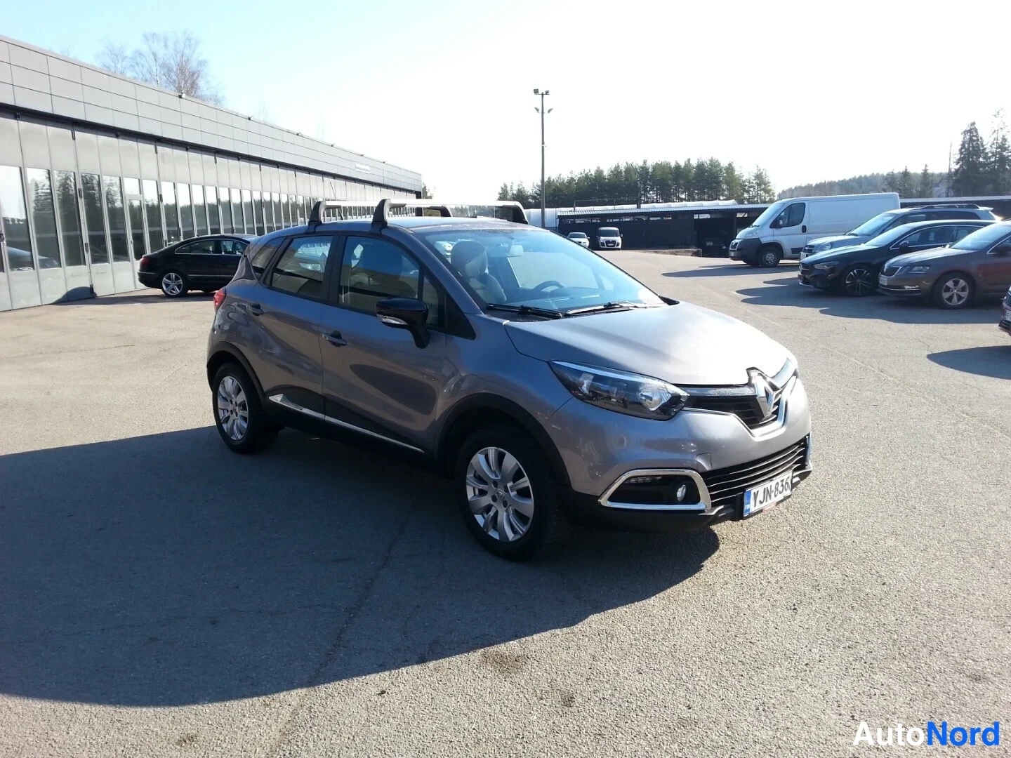 Etuviisto, nokka oikealle: Renault Captur -auto kolmannelta etusektoralta, hopeanharmaa kori, kattokaiteet, rekisterikilpi näkyvissä.