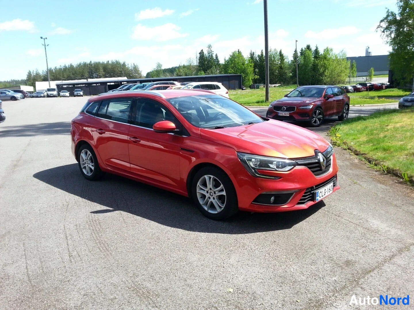 Etuviisto, nokka oikealle: Punainen Renault Megane Sport Tourer -farmari kolmanneskulmasta etunohta oikealle kääntyneenä, asfalttipihalla.