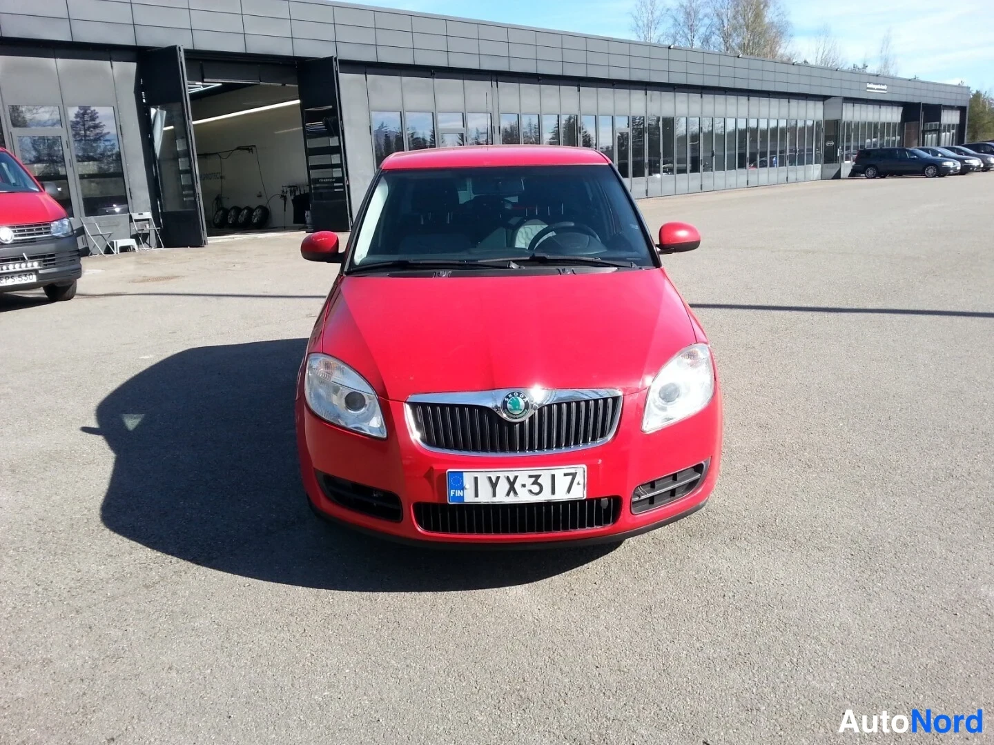 Edestä: Punainen henkilöauto edestä kuvattuna pihaalueella, rekisteritunnus.