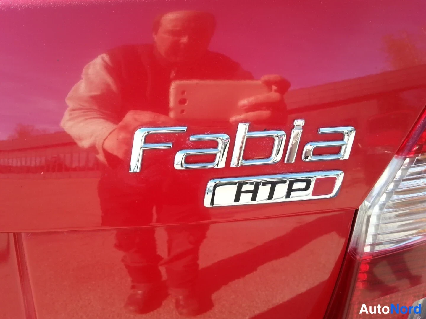 Yksityiskohta: Lähikuva punaisen Skoda Fabian takapaneelista, jossa kromikirjaimet 'Fabia' ja alla oleva 'HTP'-merkintä.