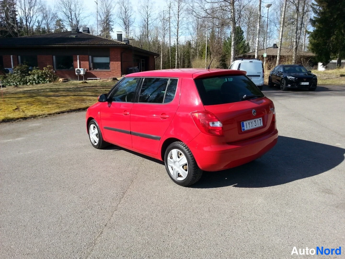 Takaviisto: Punainen Skoda Fabia -henkilöauto kuvattu takakulmasta vasemmalta, aulassaan pihamaalla rekisteritunnus näkyvissä.