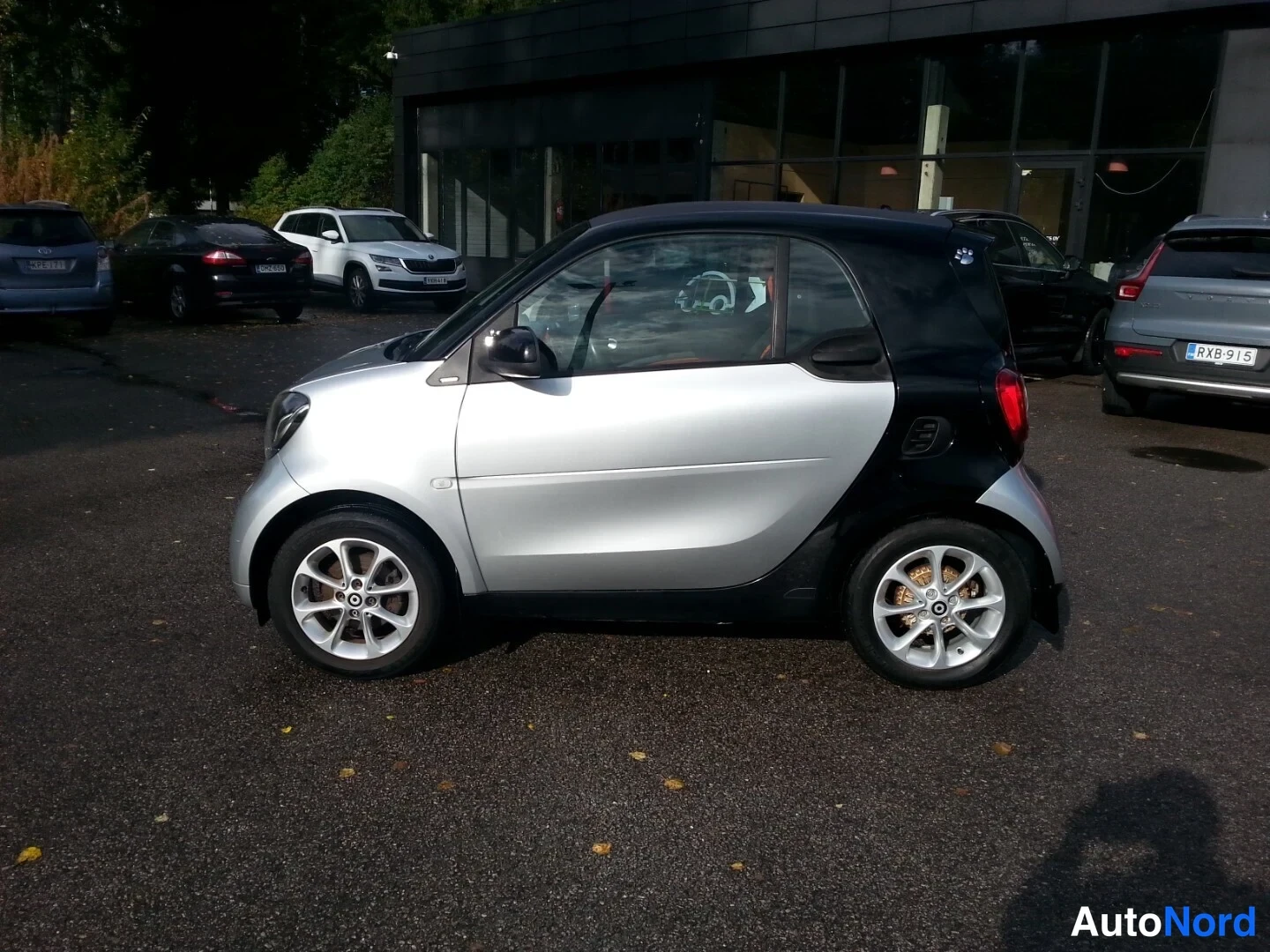Takaviisto: Hopeanmetallinhohtoinen Smart Fortwo -kaupunkiauto sivusta takaa kuvattuna, tumma katto ja takarunko, hopeat kiintevät ovipaneeleissa ja hopeaiset vanteet.