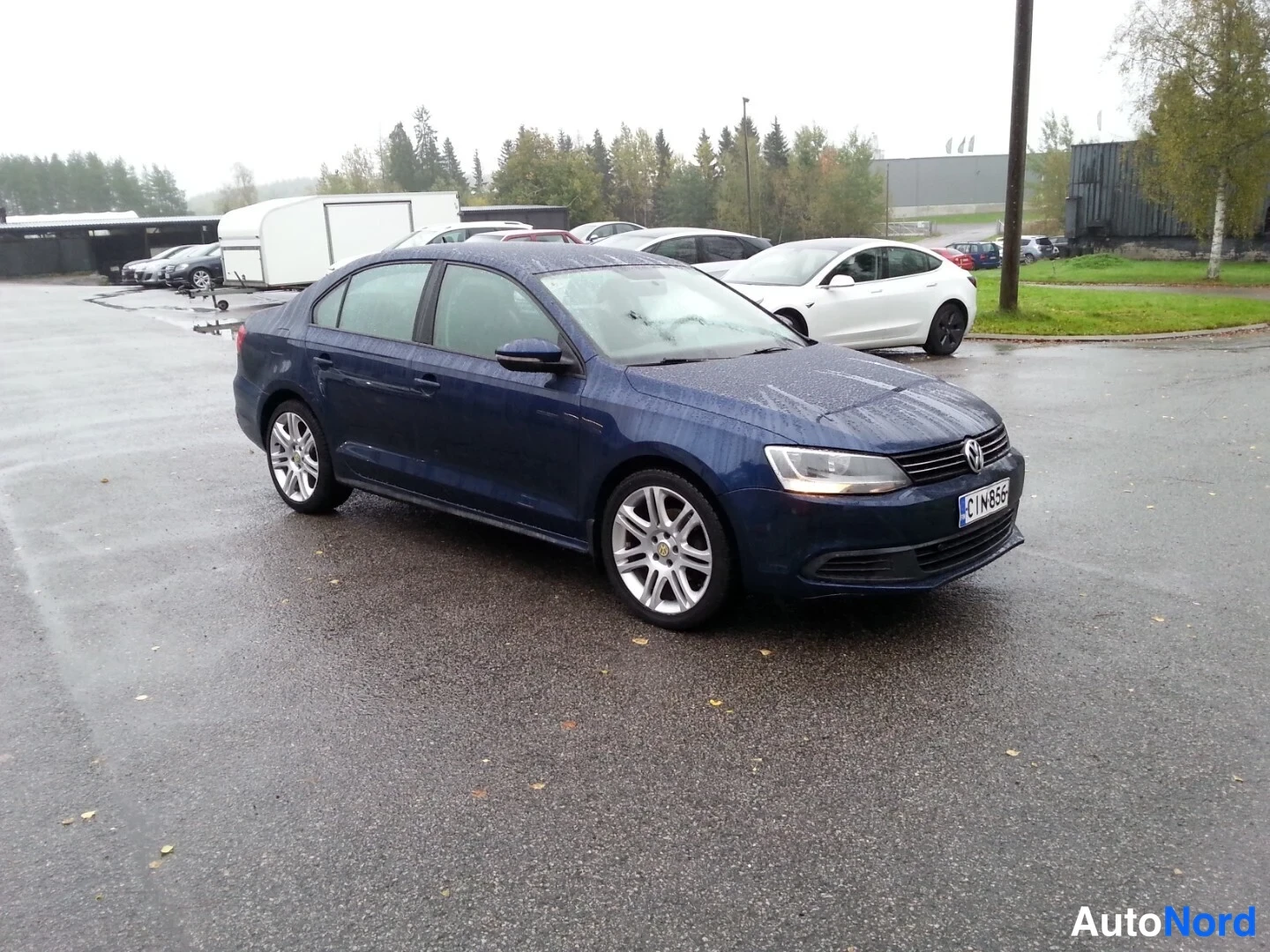 Etuviisto, nokka oikealle: Tummansininen Volkswagen Jetta -sedan vinosti edestä oikealta kuvattuna märällä parkkipaikalla.