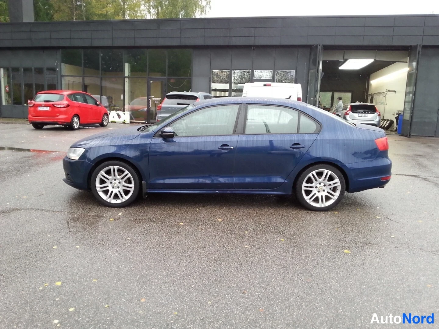 Sivulta: Tummansinisen Volkswagen Jetta -sedanin sivukuva vasemmalta katsottuna autoliikkeen edessä.