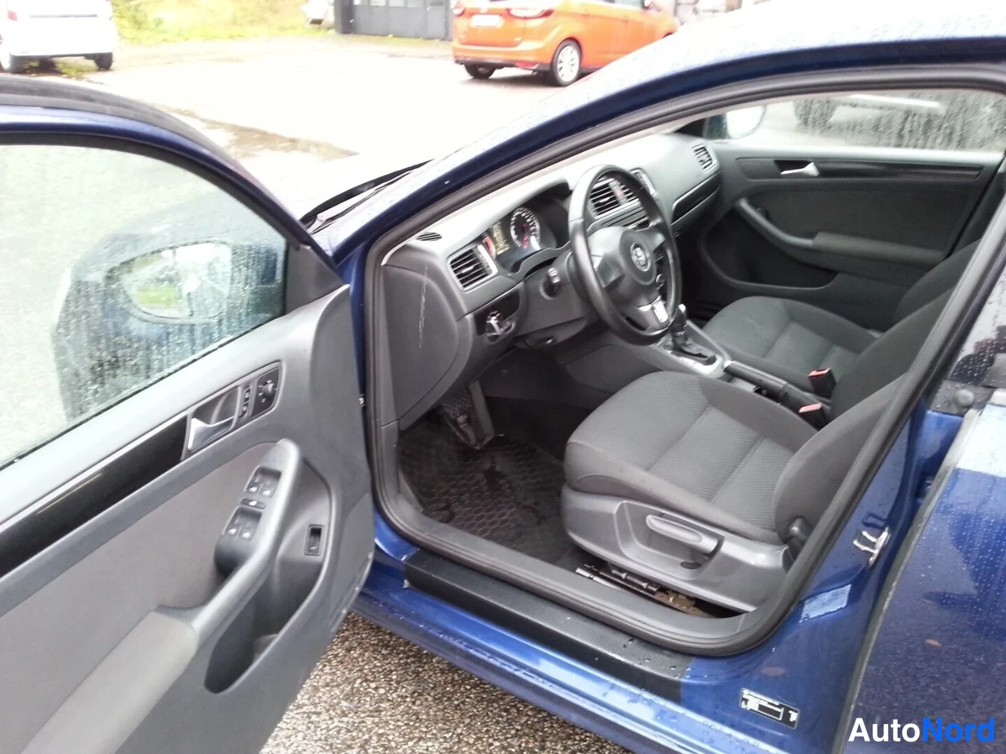 Muu: Avoimesta etuovesta näkyy Volkswagenin tumma sisätila: kori ohjauspyörä, kojelauta ja etumatkustajan istuin.