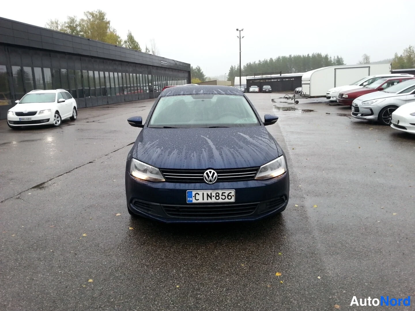 Edestä: Volkswagen Jetta edestäpäin sateisella parkkialueella, rekisteritunnus.