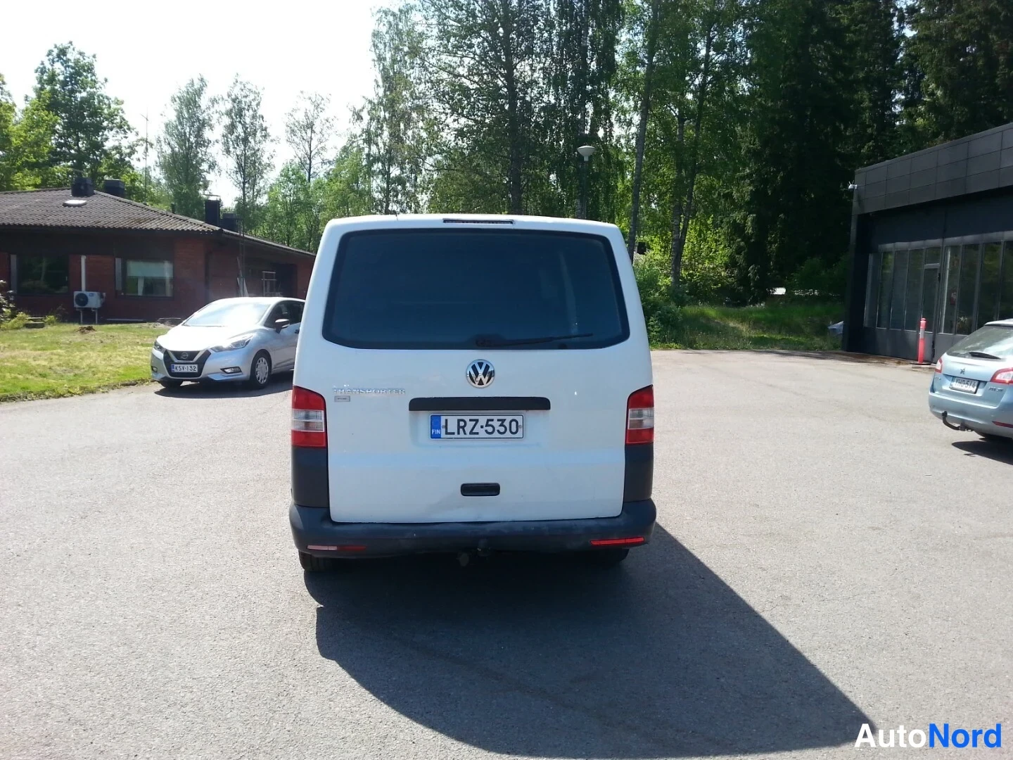 Takaa: Valkoisen pakettiauton takanäkymä, rekisteritunnus, tumma takaosa ja punaiset takavalot.