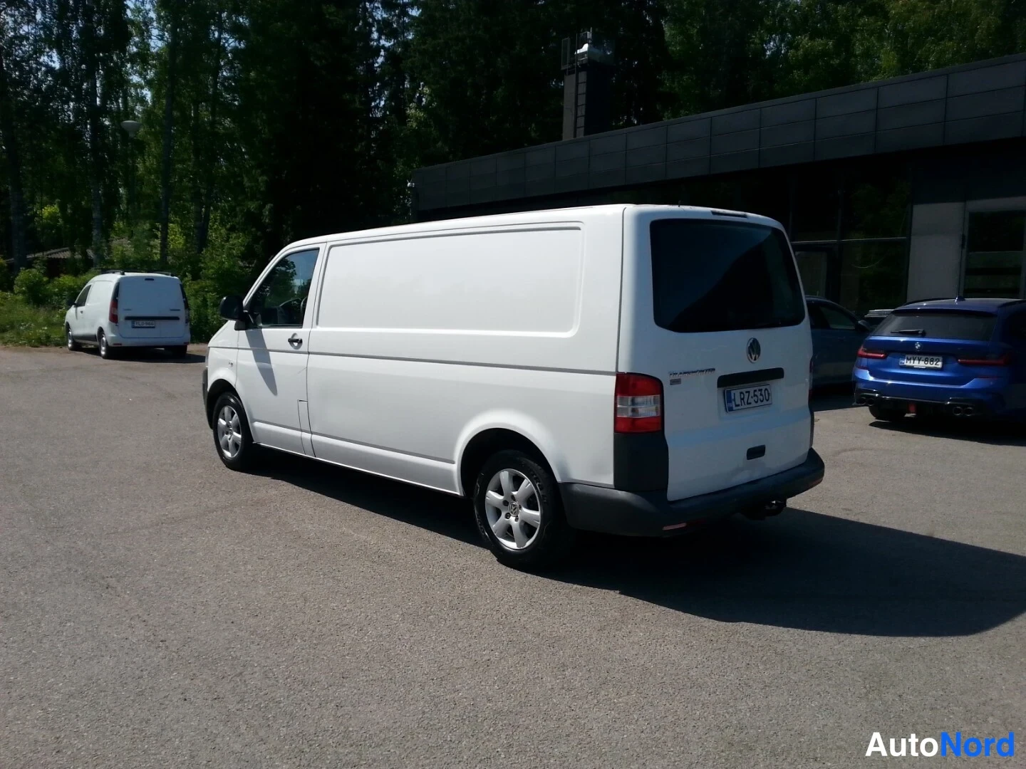Takaviisto: Valkoinen pakettiauto kulmasta takaa vasemmalta kuvattuna; rekisterikilpi, pyöränkannattaja takapuskurissa.