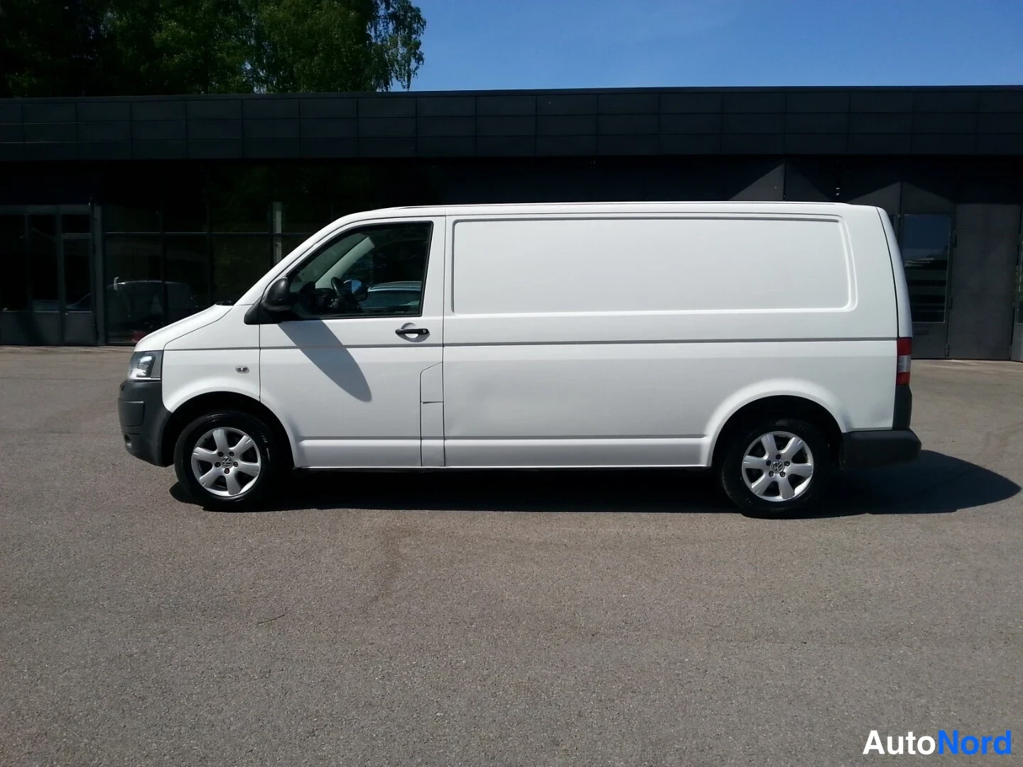 Etuviisto, nokka vasemmalle: Valkoinen pakettiauto sivusta vasen etukulma, keula kuvan vasemmassa reunassa, hopeavanteet.