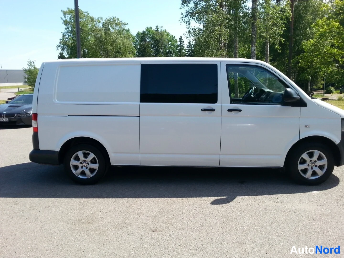 Takaviisto: Valkoinen pakettiauto oikea sivuprofiili, takana panoroitu liukuovi ja tummat lasit, hopeavanteet.