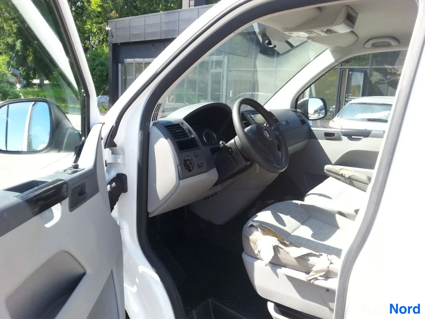 Muu: Avaudetun etuoven kautta näkyvä ohjaamo: kuljettajan penkki, ohjauspyörä, kojelauta ja keski console, istuinkankaiden välissä kulumaa.