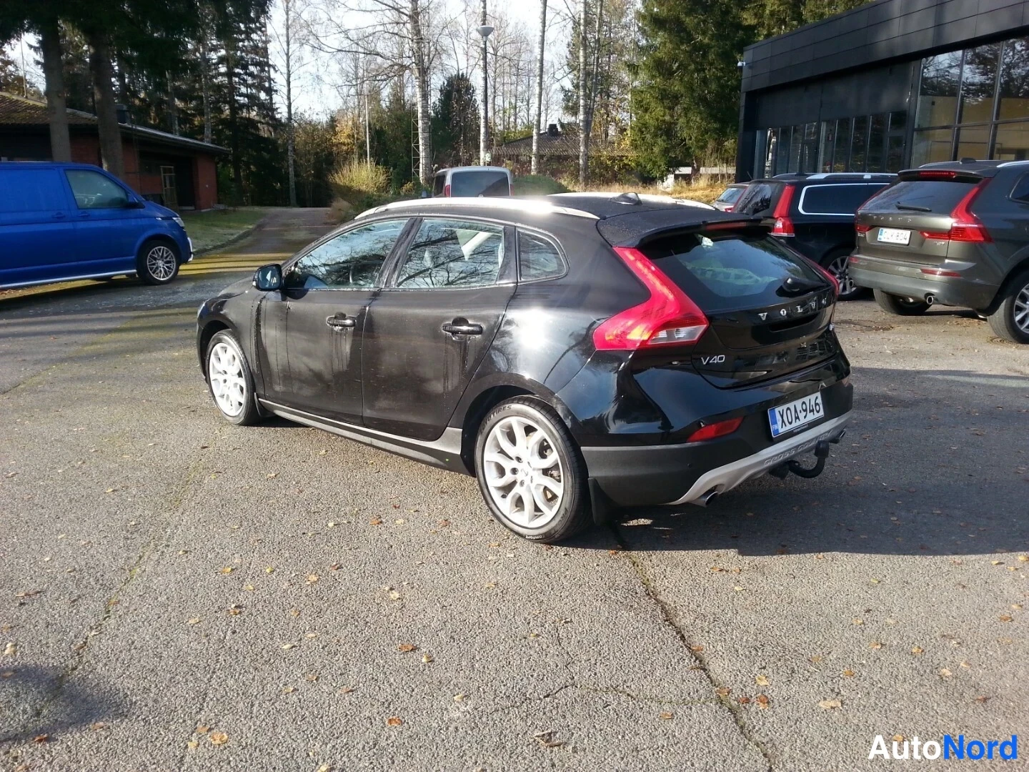 Takaviisto: Musta Volvo V40 takaa vasemmalta sivulta kuvattuna, rekisterikilpi, peräovessa V40-merkintä, kattokaiteet ja hopeiset vanteet näkyvät.