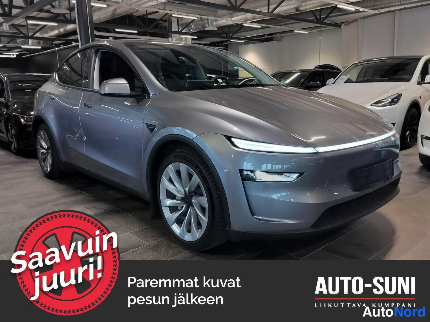Etuviisto, nokka oikealle: Hopeanharmaa Tesla Model Y etuloksu oikealta kuvattuna näyttelytilassa.