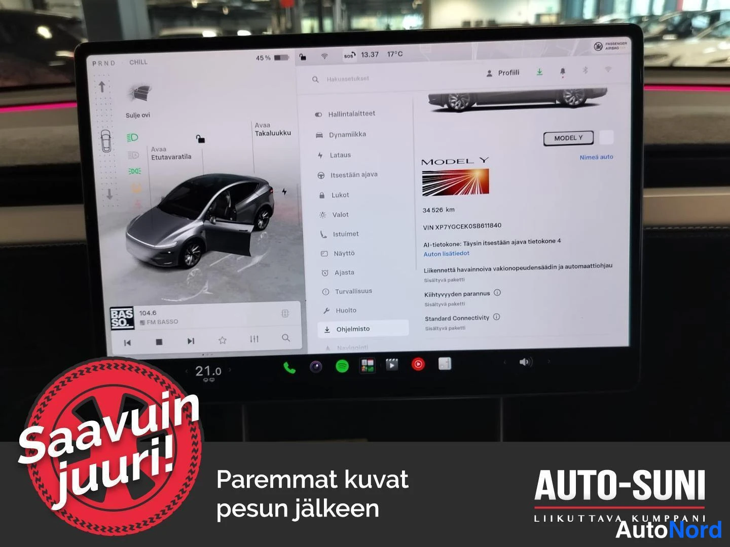 Muu: Auton keskikonsolin kosketusnäyttö lähikuvassa. Vasemmalla ajoneuvon visuaalinen hallintanäkymä ja oikealla Ohjelmiot-valikko, jossa lukee MODEL Y, 34 526 km ja