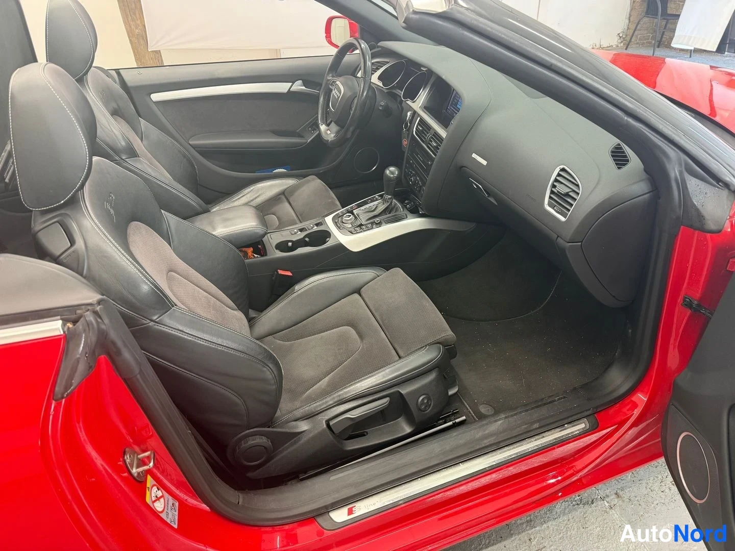 Muu: Avo-auton matkustamisto kuvattu avoimesta ovesta: mustat penkit, ratkossa Audi-logo ja automaattivaihteen valitsin, kori punainen.