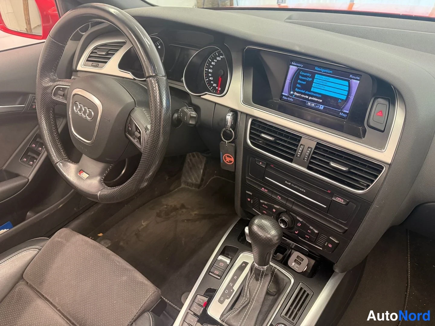 Muu: Kojelauta lähikuvassa: Audi-merkitty ohjatratti, mittaristo ja keskikonsolin näytöllä navigaatiovalikko, vaihteenvalitsin asennossa P.