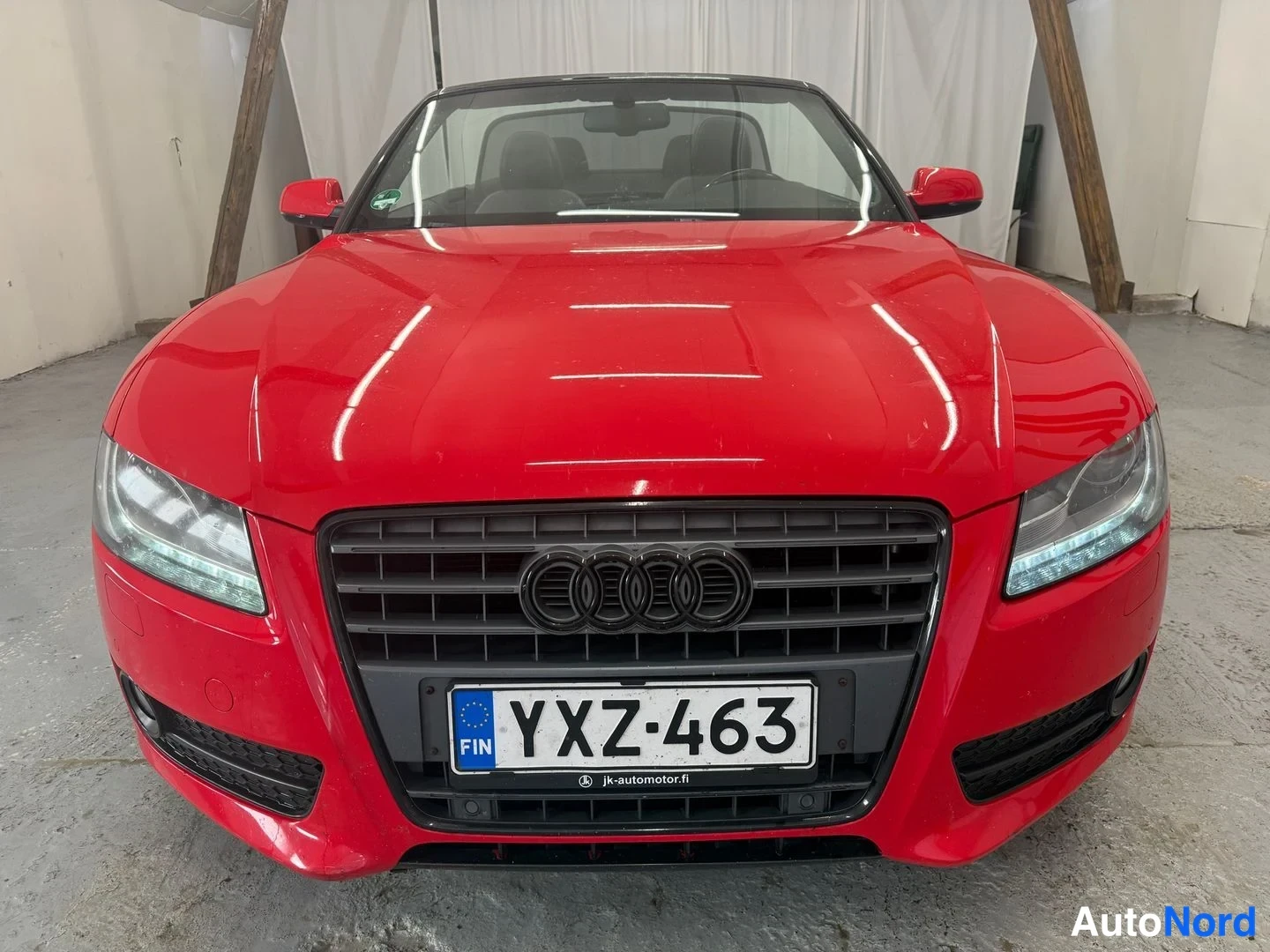 Edestä: Punaisen auton keula suoraan edestä kuvattuna, Audi-merkki säleikössä ja rekisterikilpi.