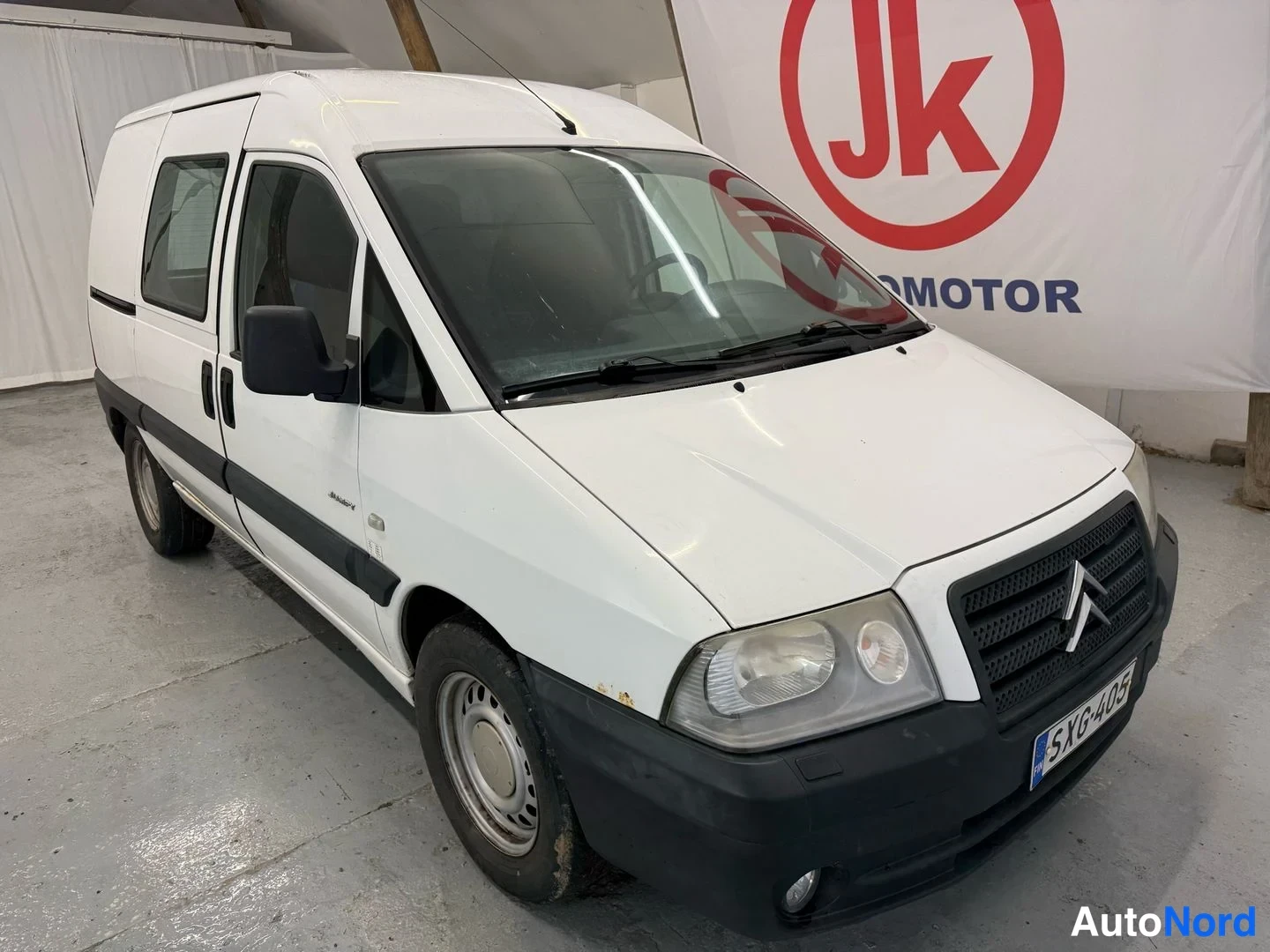 Etuviisto, nokka oikealle: Valkoinen Citroën Jumpy -pakettiauto keula oikealla, sivu ja etusäleikkö näkyvissä.