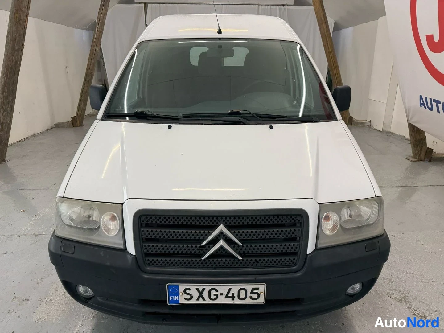 Edestä: Valkoisen Citroën Jumpy -pakettiauton keula suoraan edestä, rekisterikilpi.