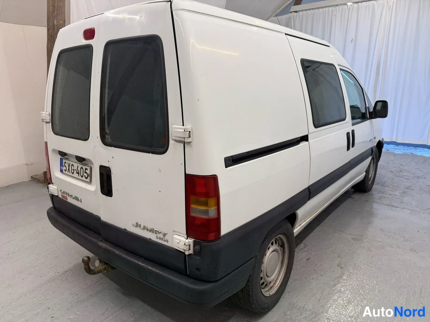 Takaviisto: Pakettiauto takaa viistosti: valkoinen Citroën Jumpy, jonka peräovissa Dual Mass -luukuissa tarrat ja rekisterikilpi.
