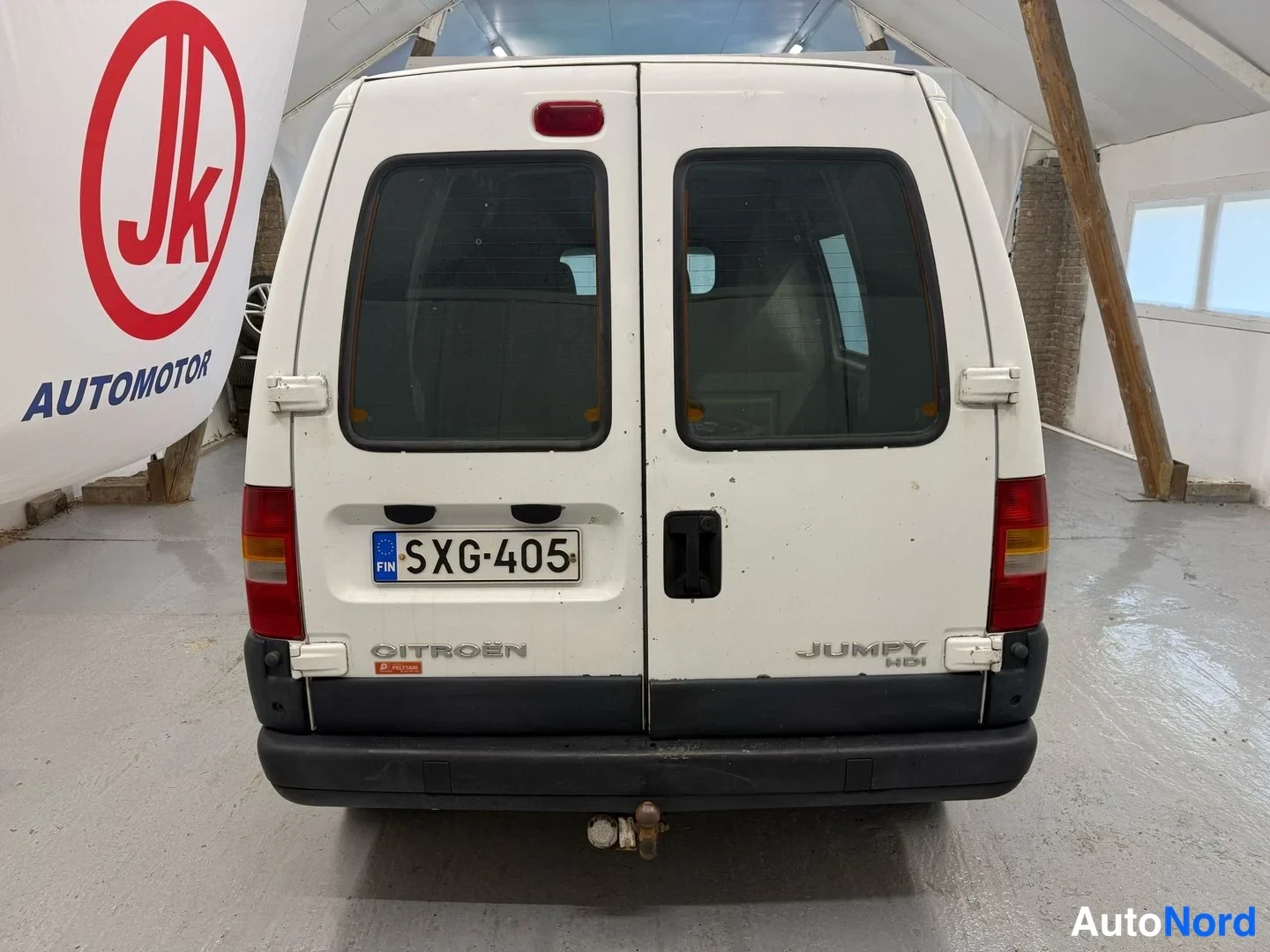 Takaa: Pakettiauto suoraan takaa: valkoinen Citroën Jumpy, jonka peräovessa tarrat ja rekisterikilpi.