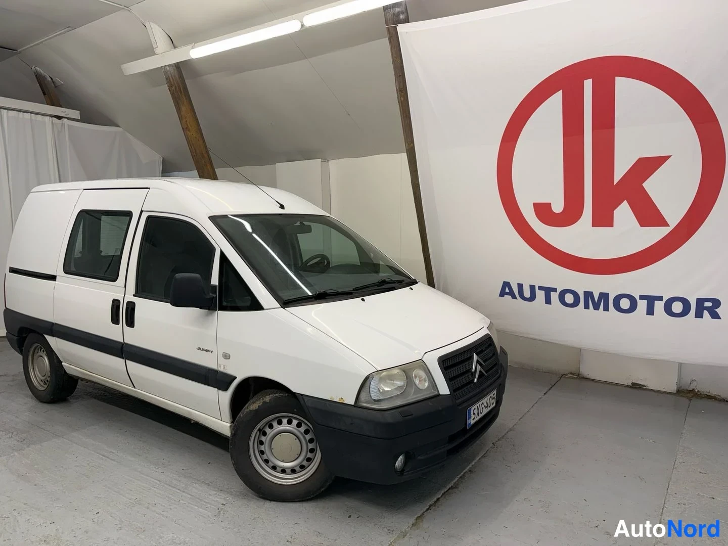 Etuviisto, nokka oikealle: Pakettiauto edestä sivusuunnasta: valkoinen Citroën Jumpy, jonka keulassa tumma etusäleikkö ja rekisterikilpi.