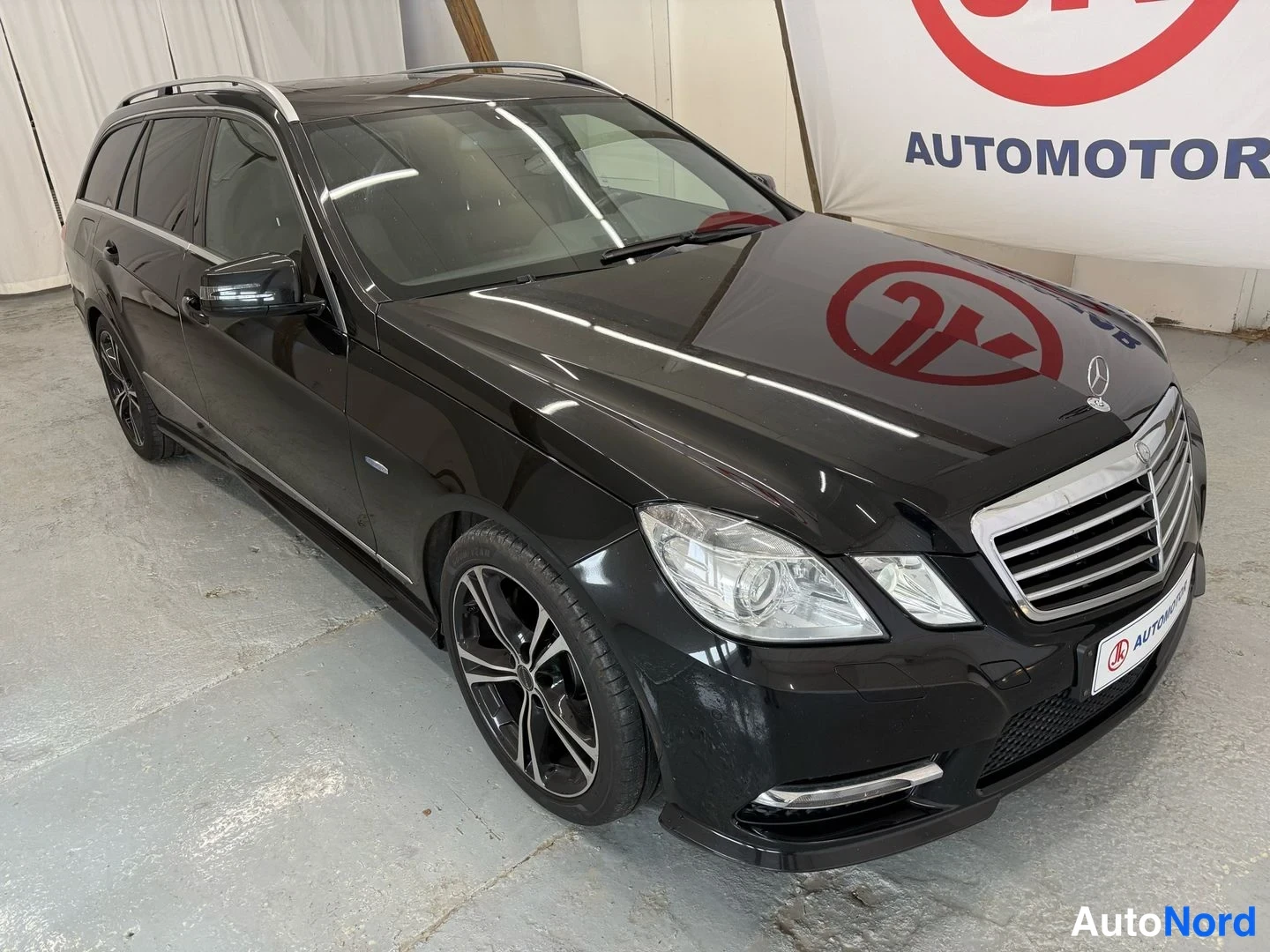 Etuviisto, nokka oikealle: Musta Mercedes-Benz farmarivaihtoauto kuvattu kolmannesvetoisesti keulasta oikealta sisätiloissa.