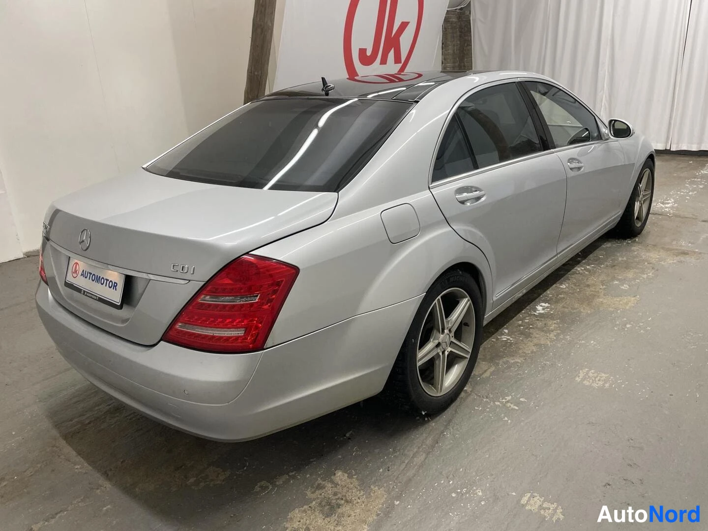 Takaviisto: Hopeanharmaa Mercedes-Benz S-sarjan sedan takaviistosta oikealta kuvattuna; takavalot, kannen merkinnät ja oikean puolen ovista ja pyörät näkyvät.