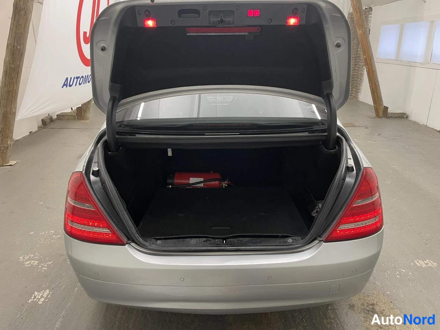 Takaa: Hopeanharmaan auton takahallin avattu takaosa suoraan takaa kuvattuna; tavaratila on tyhjä paitsi punainen sammutin on näkyvissä.