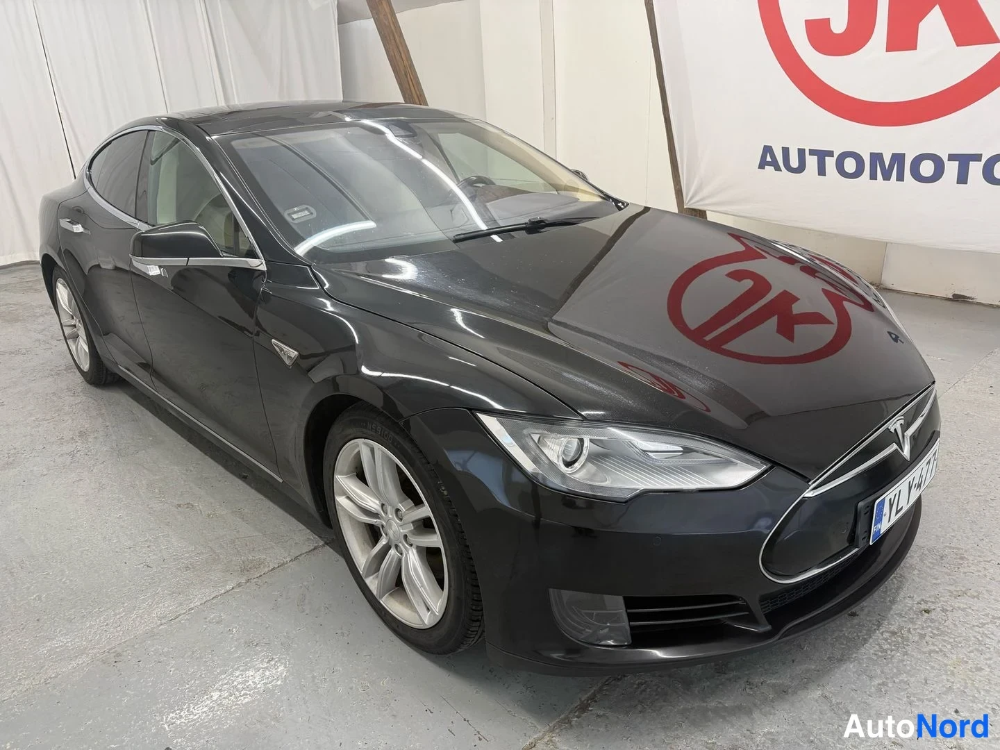 Etuviisto, nokka oikealle: Mustan Tesla Model S -sedanin etukulma vasemmasta yläkulmasta, rekisterikilpi näkyvissä.