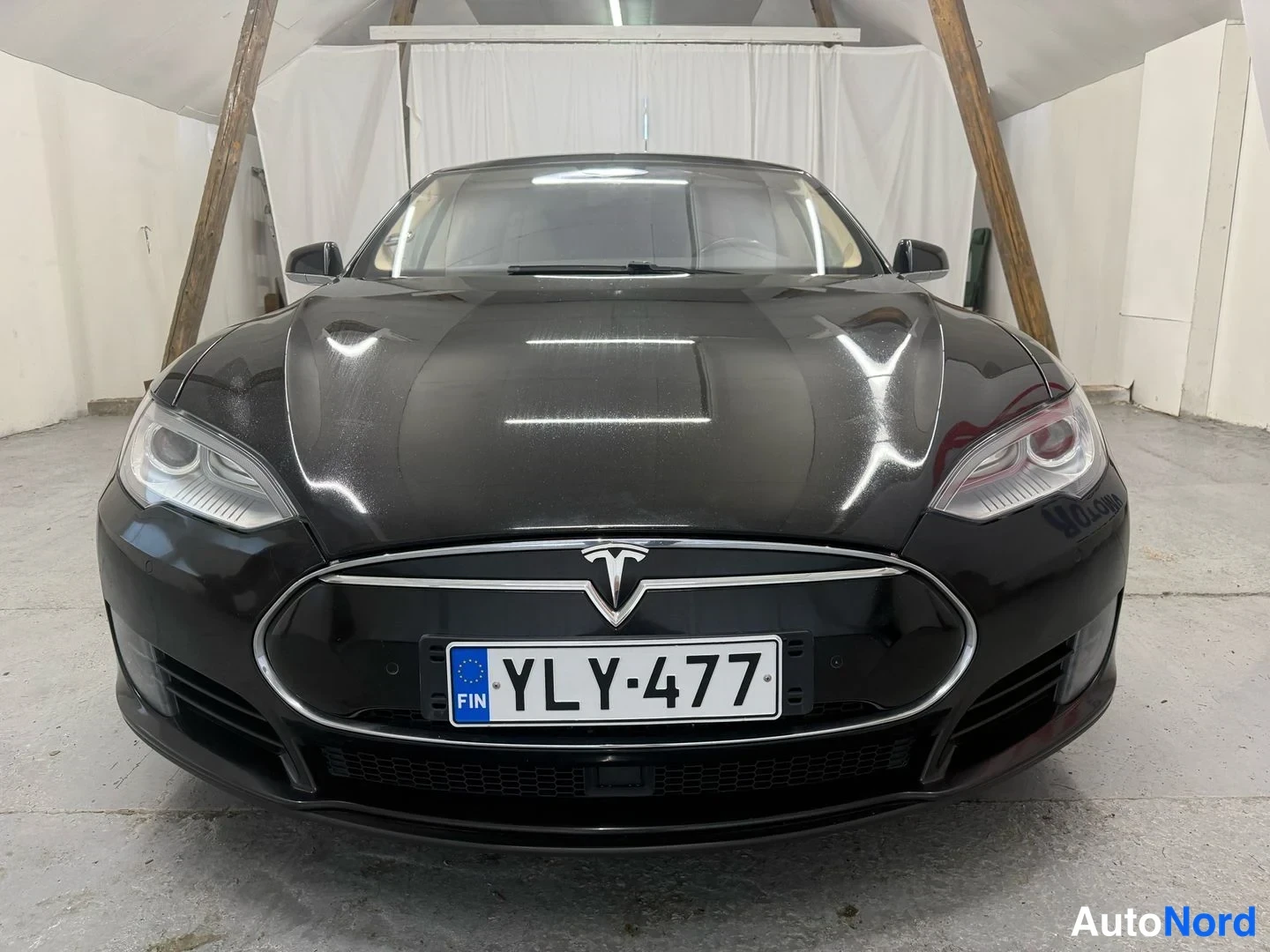Edestä: Mustan Tesla Model S -sedanin keula suoraan edestä, rekisterikilpi näkyvissä.