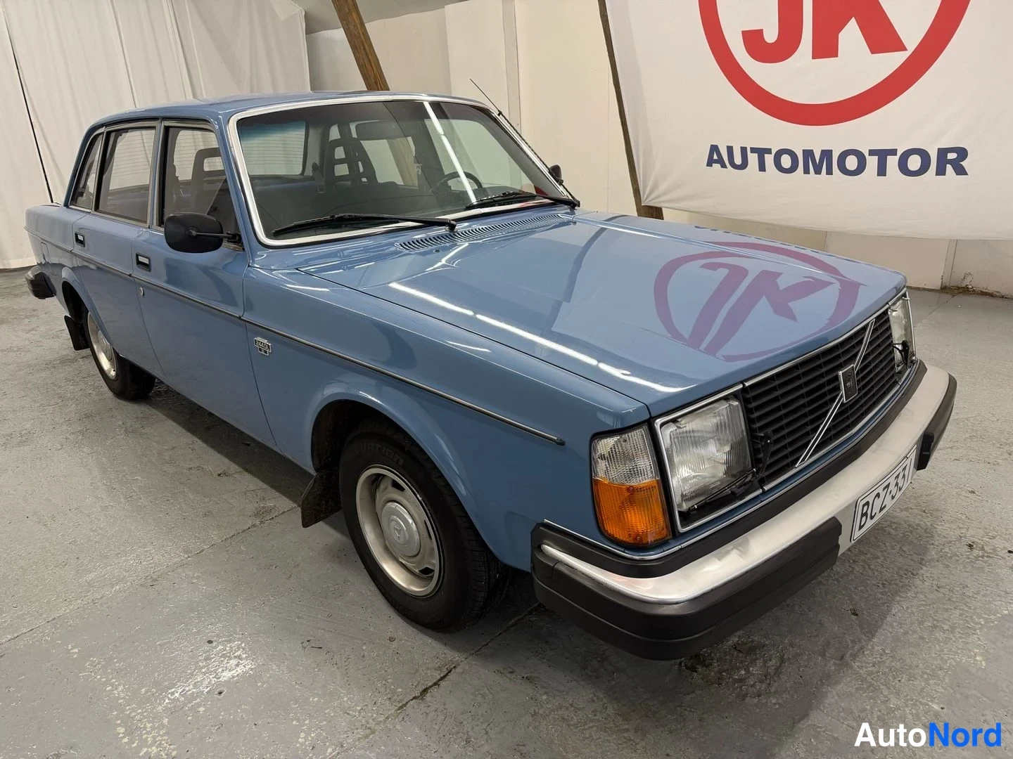 Etuviisto, nokka oikealle: Sininen Volvo 240 -sedan etukenänurkkakuvassa; etusäleikkö, ajovalot ja rekisterikilpi näkyvät.