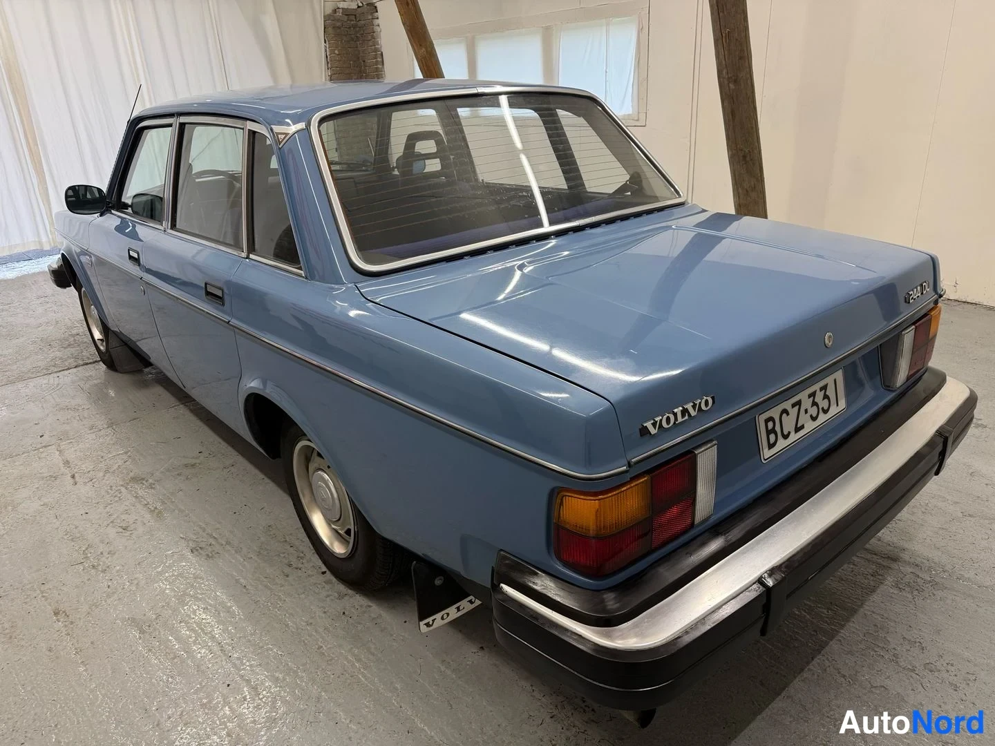 Takaviisto: Sininen Volvo 244 DL takaviistosta oikealta kuvattuna, VOLVO-merkintä ja rekisteritunnus.