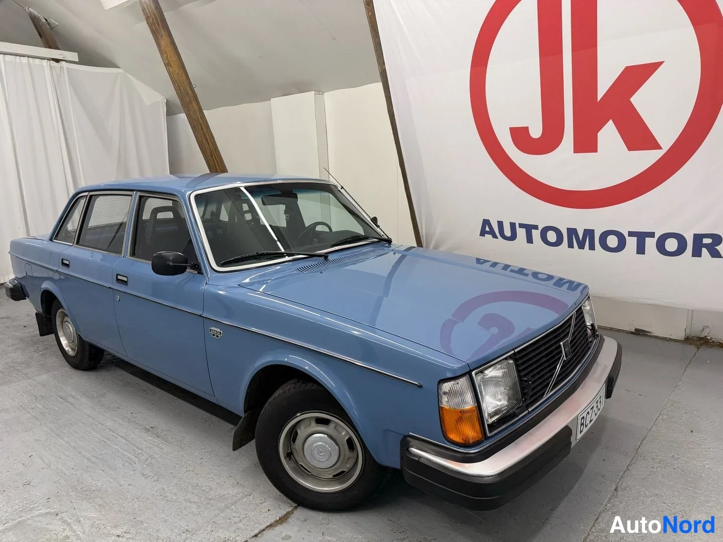 Etuviisto, nokka oikealle: Sininen Volvo 244 DL etuviistosta oikealta kuvattuna, rekisteritunnus näkyy osittain.