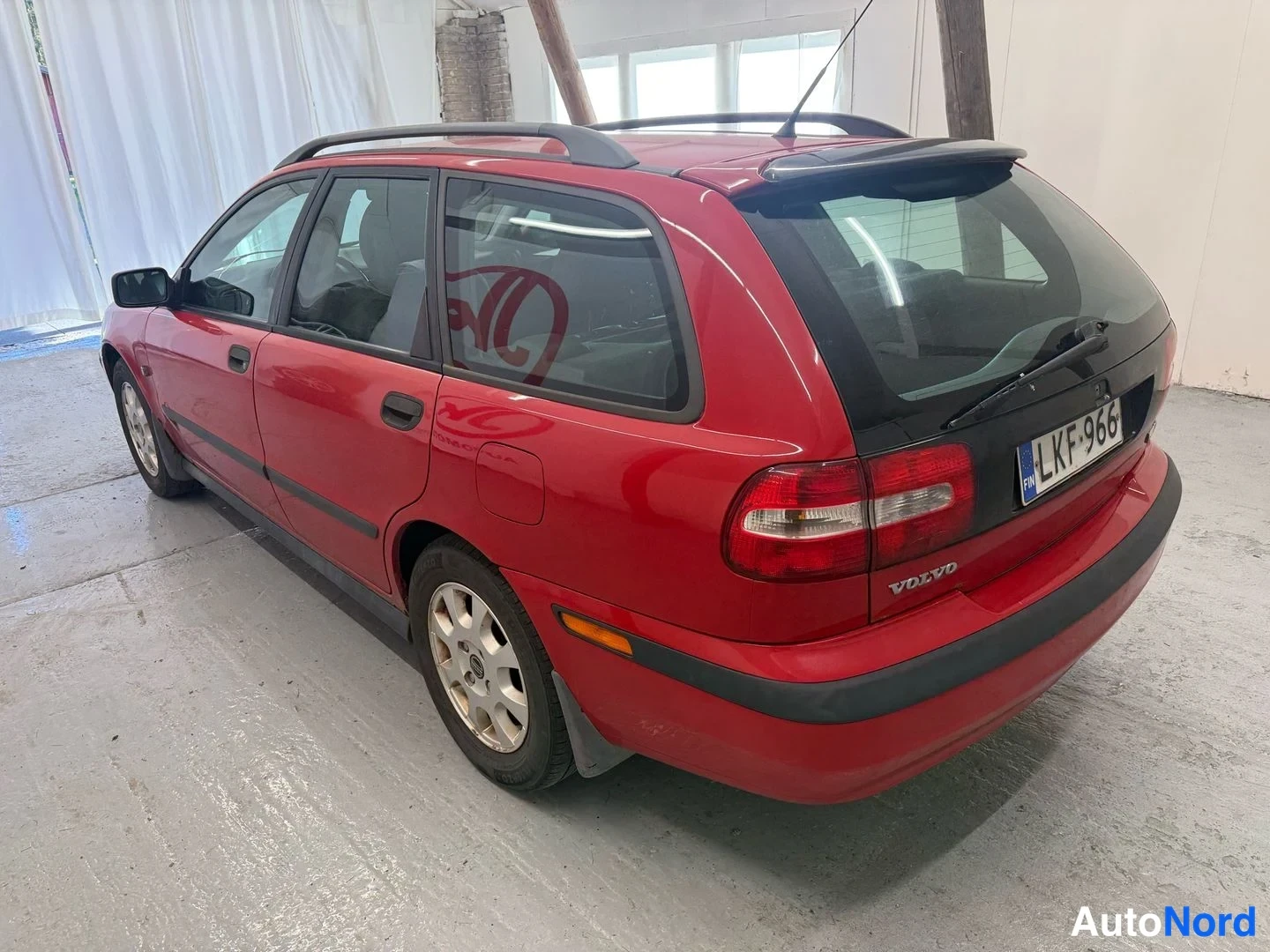 Takaviisto: Punaisen Volvo V40 -farmarin takakulmanäkyväs toiselta puolelta; VOLVO-merkintä, -rekisterikilpi ja kattokaiteet näkyvät.