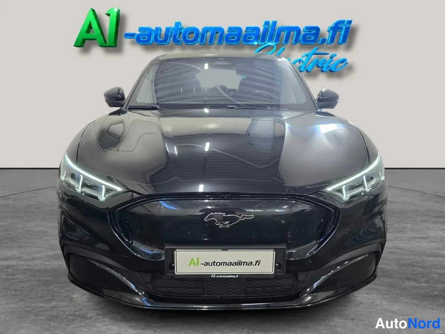 Edestä: Mustan Ford Mustang Mach-E:n suora etunäkymä, keulalla Ford Mustang -tunnus ja A1-automaailma.fi -kyltti.