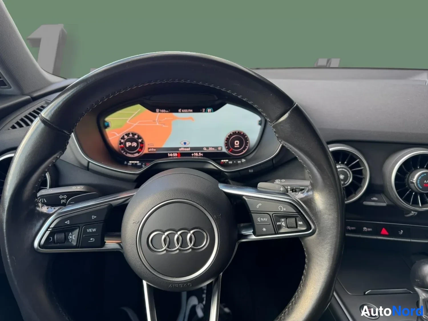 Etuviisto: Audi-ohjauspyörä ja digitaalinen mittaristo, jonka näytöllä navigointikartta ja nopeusmittari; vasemmalla VIEW-napit ja oikealla NAV/Media-ohjaimet.