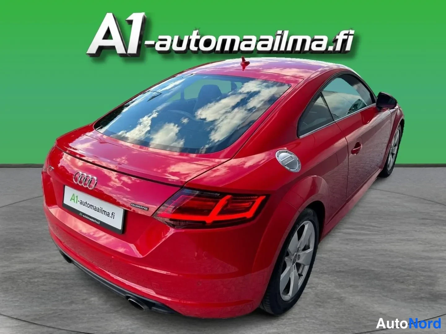 Takaviisto: Punaisen Audi TT Coupén takaosan kolmannesvasen näkymä: takavalot, Audi-merkki ja nokkaistukea muistuttava takaluukku näkyvät vihreää taustaa vasten.